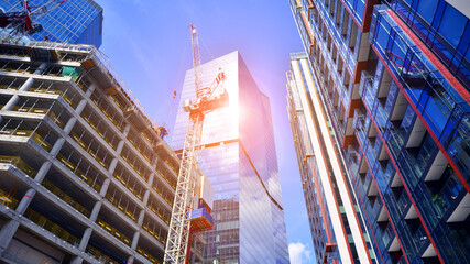 Crane on the construction site in a site surrounded by the high buildings. Office building under construction in the vicinity of high apartment buildings and office building.