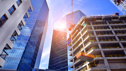 Crane on the construction site in a site surrounded by the high buildings. Office building under construction in the vicinity of high apartment buildings and office building.