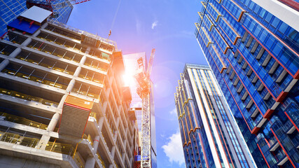 Crane on the construction site in a site surrounded by the high buildings. Office building under construction in the vicinity of high apartment buildings and office building.