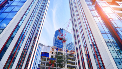 Crane on the construction site in a site surrounded by the high buildings. Office building under construction in the vicinity of high apartment buildings and office building.