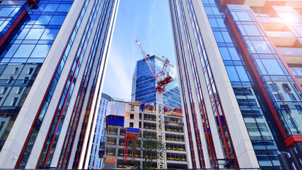 Crane on the construction site in a site surrounded by the high buildings. Office building under construction in the vicinity of high apartment buildings and office building.