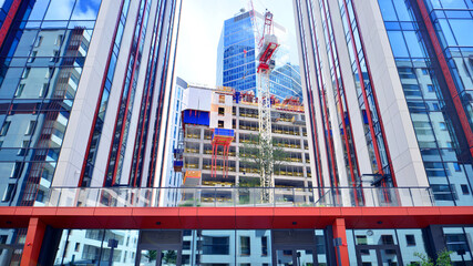 Crane on the construction site in a site surrounded by the high buildings. Office building under construction in the vicinity of high apartment buildings and office building.