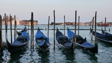 Gondolas docked in Venice with a gondolier steering across calm waters. In the background, the Church of San Giorgio Maggiore rises with its bell tower&mdash;capturing the serene and iconic spirit of the ci