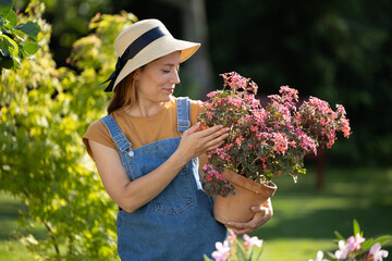 Pretty female gardener admiring pot with flowers in hands