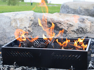 Burning coals in black metal grill. Barbecue grill with glowing flames, positioned outdoors amidst...