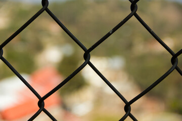 Primer plano de malla ciclónica metálica negra con fondo muy desenfocado y efecto bokeh.