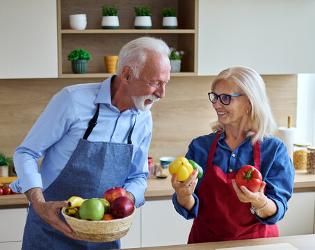Portrait of happy senior mid aged mature couple prepering meal with fresh vegatebles in kitchen at hpme