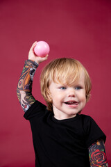 Little boy in studio on red background playing, eating, crying, smiling in black t-shirt with artificial tattoos on his arms