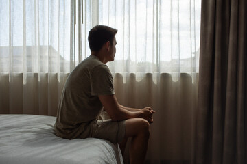 Thoughtful alone man in his bedroom looking out his window thinking about life future, worries, fears  