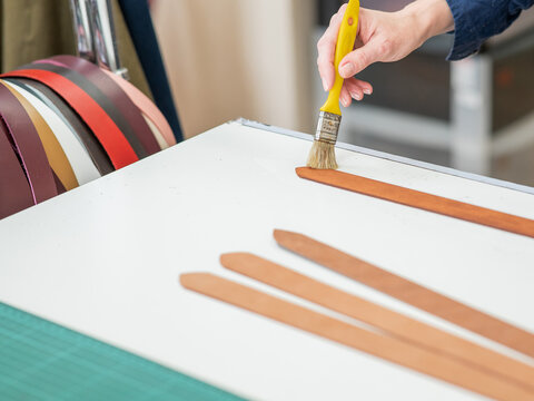 A craftsman uses a brush to cover leather parts. 
