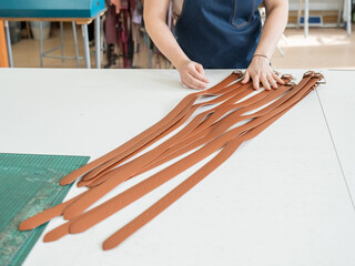 Caucasian woman makes belts from genuine leather in a workshop. 