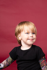 Naklejka premium Little boy in studio on red background playing, eating, crying, smiling in black t-shirt with artificial tattoos on his arms