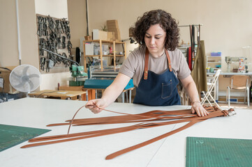 Caucasian woman makes belts from genuine leather in a workshop. 