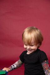 Naklejka premium Little boy in studio on red background playing, eating, crying, smiling in black t-shirt with artificial tattoos on his arms