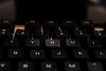 Close-up of black keyboard with "YOU" keys highlighted. Conceptual image with motivational or romantic tone, emphasizing personal importance.