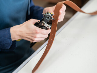 A woman makes holes in a leather belt. Leatherworker's workshop. 