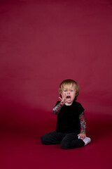 Little boy in studio on red background playing, eating, crying, smiling in black t-shirt with...
