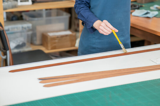A craftsman uses a brush to cover leather parts. 