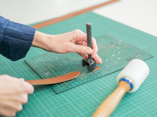 Woman tanner processes the edges of a leather belt in a workshop. 