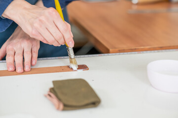 A craftsman uses a brush to cover leather parts. 