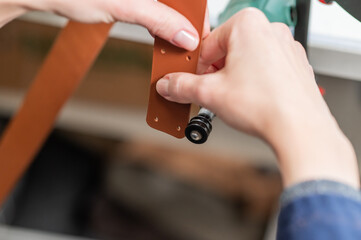 Leatherworker grinding the edge of a strip of leather for a belt in the workshop. 