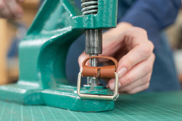 A woman attaches accessories to a leather belt. Leatherworker's workshop. 