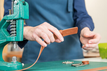 A woman attaches accessories to a leather belt. Leatherworker's workshop. 