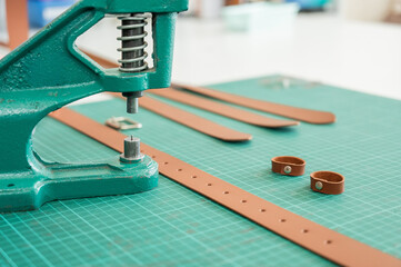 A woman attaches accessories to a leather belt. Leatherworker's workshop. 