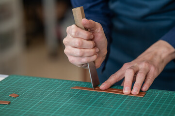 Woman tanner processes the edges of a leather belt in a workshop. 