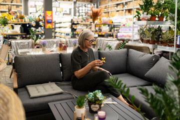 Woman sitting on a gray sectional sofa while exploring home decor options in a vibrant store during...