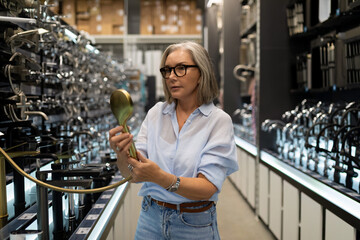 Woman exploring modern kitchen fixtures in a showroom, engaging with a stylish faucet in a...