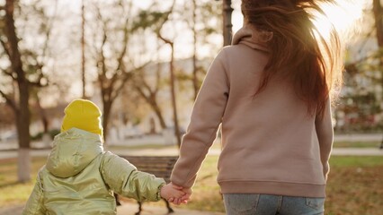 Fototapeta premium little child kid holding mother hand. closeup hands glare sun. child hand holding mom. child walk with parent park. chidhood dream. weekend park with mom. happy family vacation. walk city park sunset