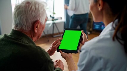 Elderly personalized medicine. A female healthcare professional helps an elderly man use a tablet with a green screen, likely for health monitoring or remote consultation.  - Powered by Adobe