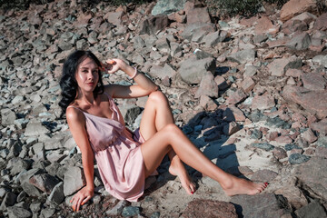 Young sexy beautiful woman is sitting on the rocks and enjoys relaxation, the warm sun and nature. Wellness, tourism, holidays, vacation and weekends.	