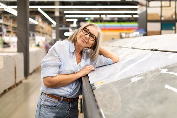 Smiling woman in glasses enjoys browsing materials in a modern home improvement store