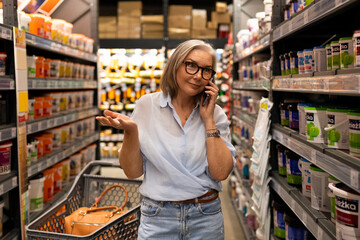 Woman shopping in a grocery store aisle while talking on the phone during afternoon hours