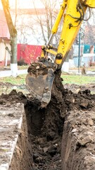 Fototapeta premium Yellow excavator digs a trench in the ground