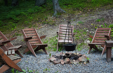 Campfire seating area with wooden chairs and cooking pot in a natural setting