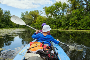 Two people paddle a kayak on a calm river surrounded by green trees. Outdoor adventure, summer...