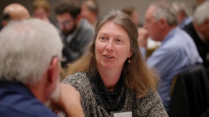 Medium shot of a group discussion among energycoop members at the annual meeting focusing on one individual sharing ideas while the rest of the crowd forms a gentle blurred