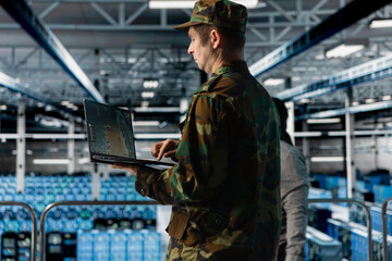 Military officer in data center monitoring warfare drone telemetry on laptop dashboard. IT...