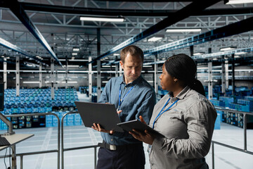 Server room coworkers doing brainstorming, backing up storage arrays using software on laptop. Team...