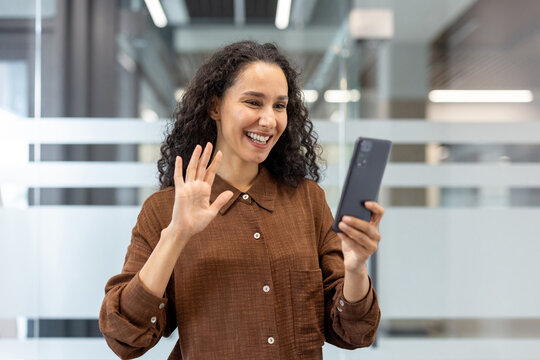 Smiling woman waving during a video call on her smartphone in office setting