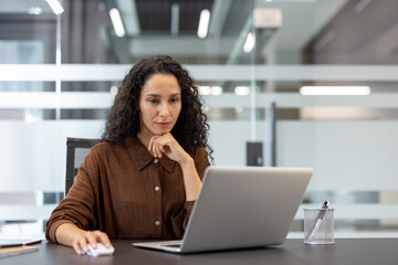 Focused woman working on a laptop at a modern office workspace