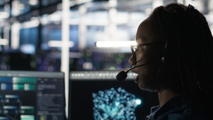 Data center employee uses audio headset and visual programming dashboard to troubleshoot client reported issues. Server farm technician looks at node tree interface, talking in microphone