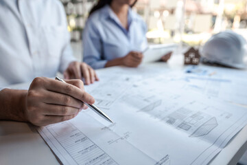 Team of architects or engineering consulting and analyzing working on objects tools and construction drawings inspection, discussing planning new architectural project on blueprint and model house