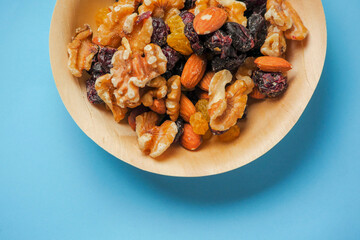 A bowl of nuts and dried fruit on a blue medical background. The bowl is made of wood and the food is colorful. Healthy diet add on. Eat natural food concept.