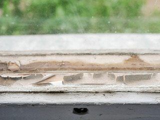 An old wooden window with peeling paint and wood. The window is dirty and has a lot of wood chips...
