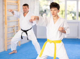 Adult man and boy teen karatekas train karate technique in studio