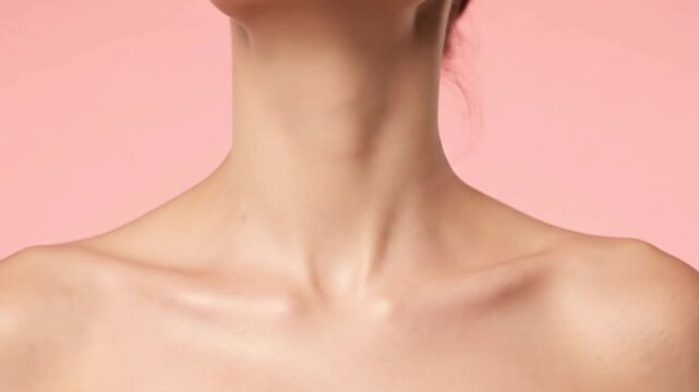 Womans bare neck  shoulders against a pink background exposing collarbones
